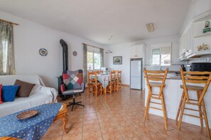 A living room with a sofa, a dining table with chairs, a kitchen area with cabinets and a refrigerator.