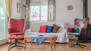A living room with a sofa, two chairs, a table, a clock, a plate, and a chimney.