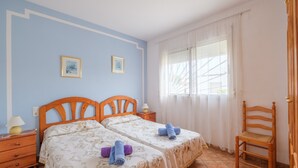 A bedroom with two beds, a wooden chair, a nightstand, and a window with curtains.