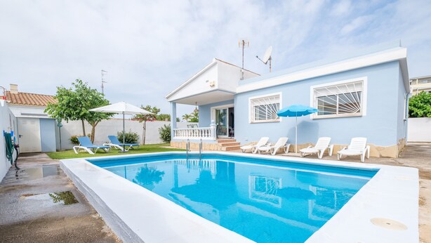A swimming pool with lounge chairs, a covered patio, and a house with a blue exterior.