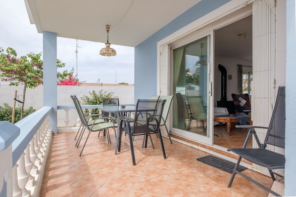 A balcony with a table and chairs, a sliding glass door leading to an interior room, and a view of the outside.
