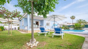 A house with a pool, blue chairs, and a tree in the yard.