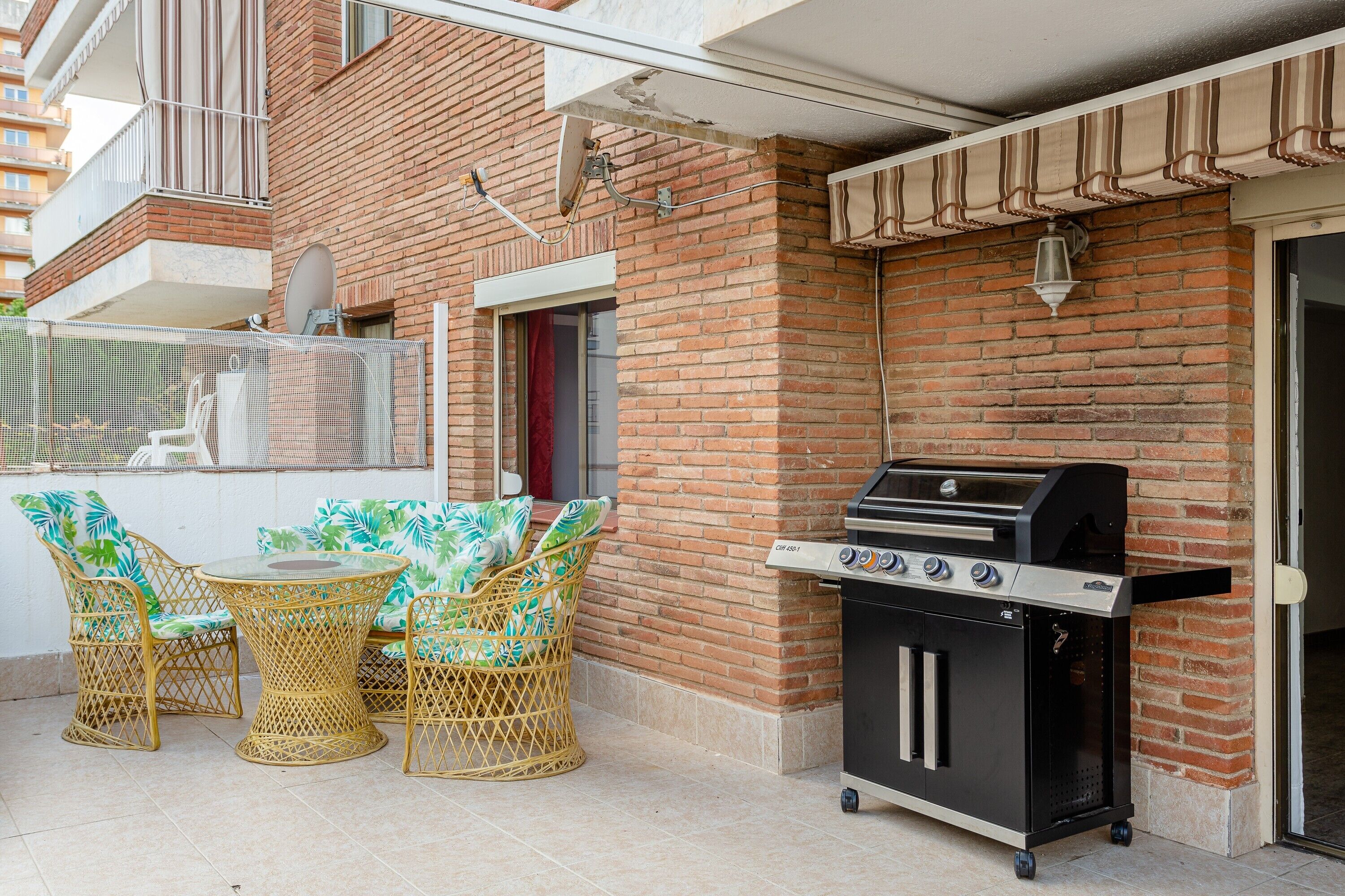 A patio with a grill, wicker chairs, and a table.