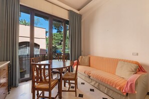 A room with a dining table, chairs, a sofa, and a view through a large window.