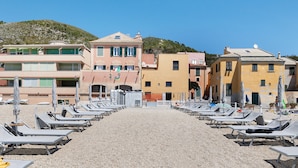 Um hotel à beira-mar com fileiras de espreguiçadeiras, uma praia de seixos e edifícios com varandas.