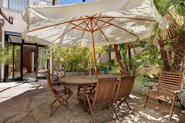 Une terrasse extérieure avec une table ronde en bois, quatre chaises en bois et un grand parasol blanc.