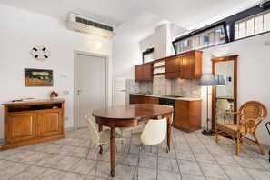 Une cuisine équipée d’une table à manger, de chaises, de meubles de rangement en bois, d’un réfrigérateur blanc et d’un sol carrelé.