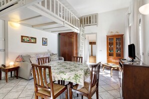 Un espace repas comprenant une table, des chaises, un canapé, un meuble et un escalier.