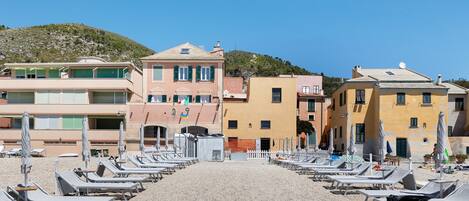 A beachside hotel with rows of sun loungers, a pebble beach, and buildings with balconies.
