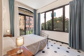 Une chambre d’hôtel avec un lit, une lampe de chevet, une fenêtre avec des rideaux et une vue sur les bâtiments environnants.