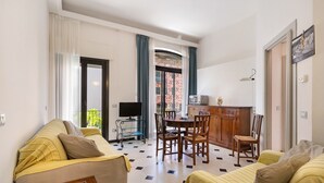 Habitación de hotel con sofá, mesa de comedor con sillas, televisor y zona de cocina.