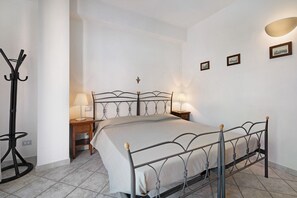 A bedroom with a metal bed frame, two bedside tables with lamps, a wooden nightstand, and a coat rack.