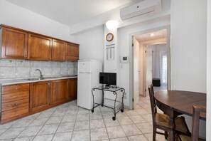 A kitchen with wooden cabinets, a white refrigerator, a small black TV on a metal cart, and a dining table with chairs.