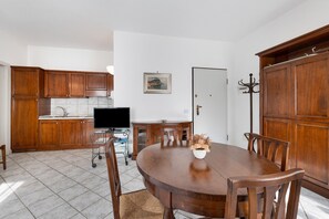 Une cuisine avec des meubles en bois, une table à manger avec des chaises, un téléviseur et un porte-manteau.