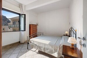 Un dormitorio con cama, cómoda, mesita de noche con lámpara, ventana y vista a un balcón.
