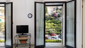 Ein Zimmer mit Fernseher auf einer Glastisch, einem Korbwicker-Korb und Blick auf einen Parkplatz mit Autos und Grünflächen.