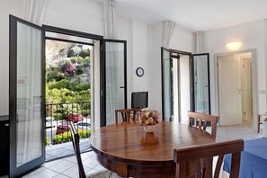 Un comedor con una mesa de madera, sillas, un jarrón de flores y un televisor sobre un mueble.
