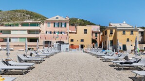 A beachside hotel with rows of sun loungers, a pebble beach, and buildings with balconies. - Pet-Friendly Apartment "18 Mehari" with Balcony & Wi-Fi (Varigotti)