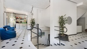 A modern lobby with a geometric floor pattern, a staircase, a reception desk, and a blue seating area. - Pet-Friendly Apartment "18 Mehari" with Balcony & Wi-Fi (Varigotti)