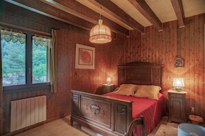 A wooden-paneled bedroom with a bed, a nightstand, a radiator, and a window with lace curtains.