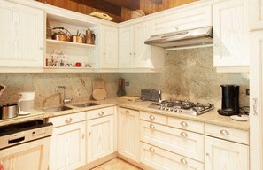 A kitchen with white cabinetry, a stainless steel sink, a Bosch dishwasher, a gas stove, and a coffee maker.
