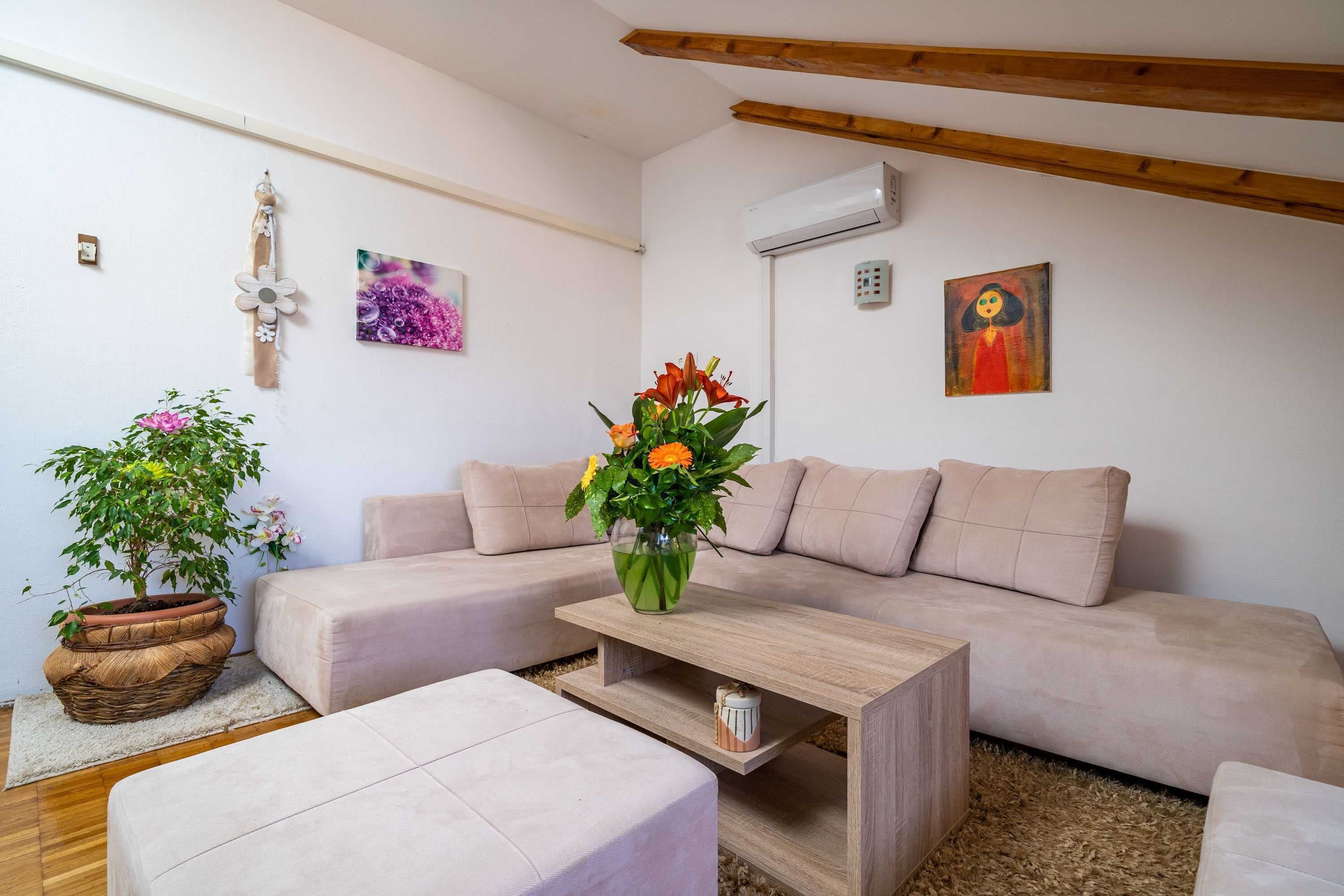 Una sala moderna con un sofá beige, una mesa de centro de madera y una planta en maceta.