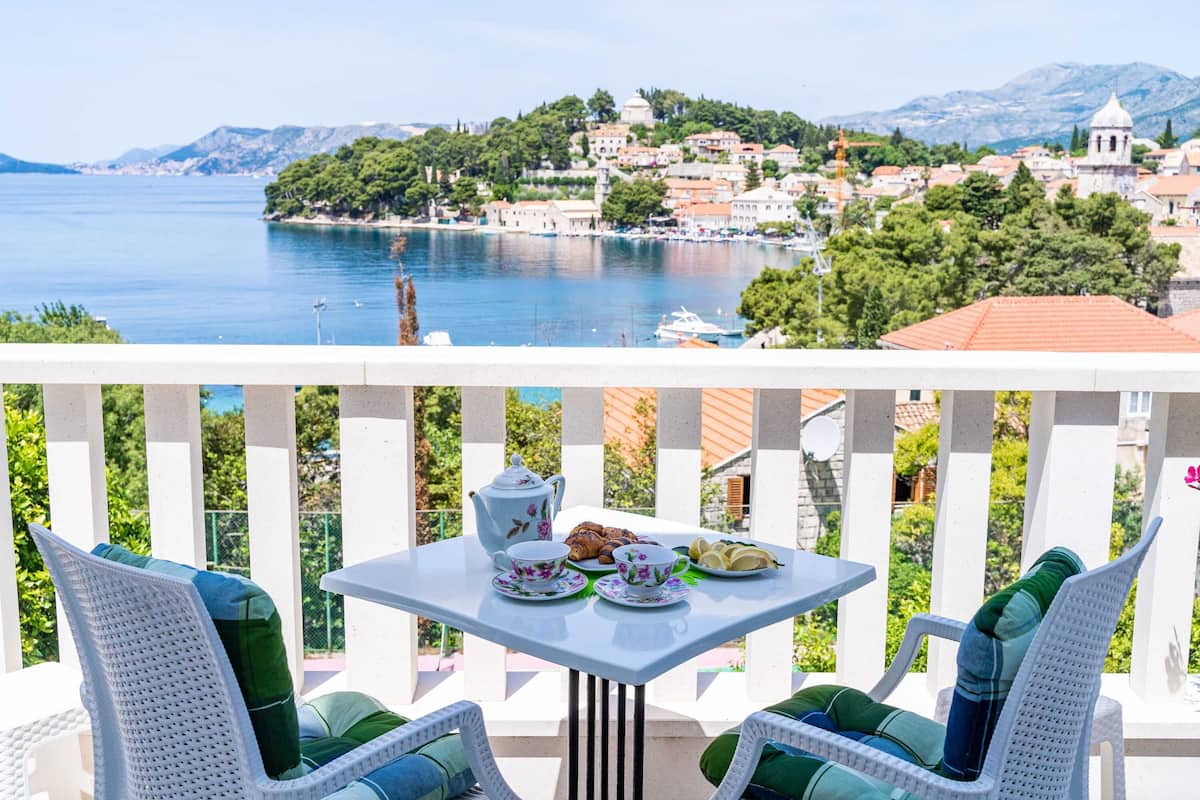 A balcony with a table set for tea, overlooking a coastal town.