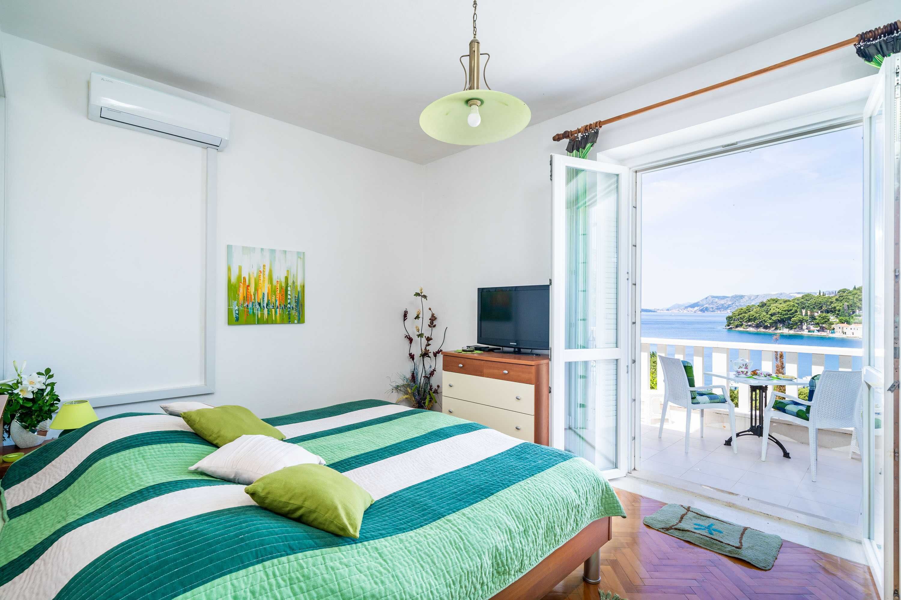 A bedroom with a bed, a TV, a balcony with chairs, and a painting on the wall.