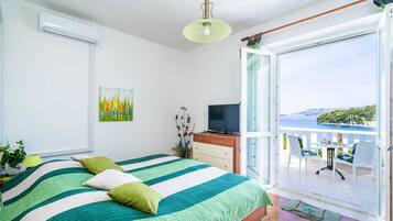 A bedroom with a bed, a TV, a balcony with chairs, and a painting on the wall.