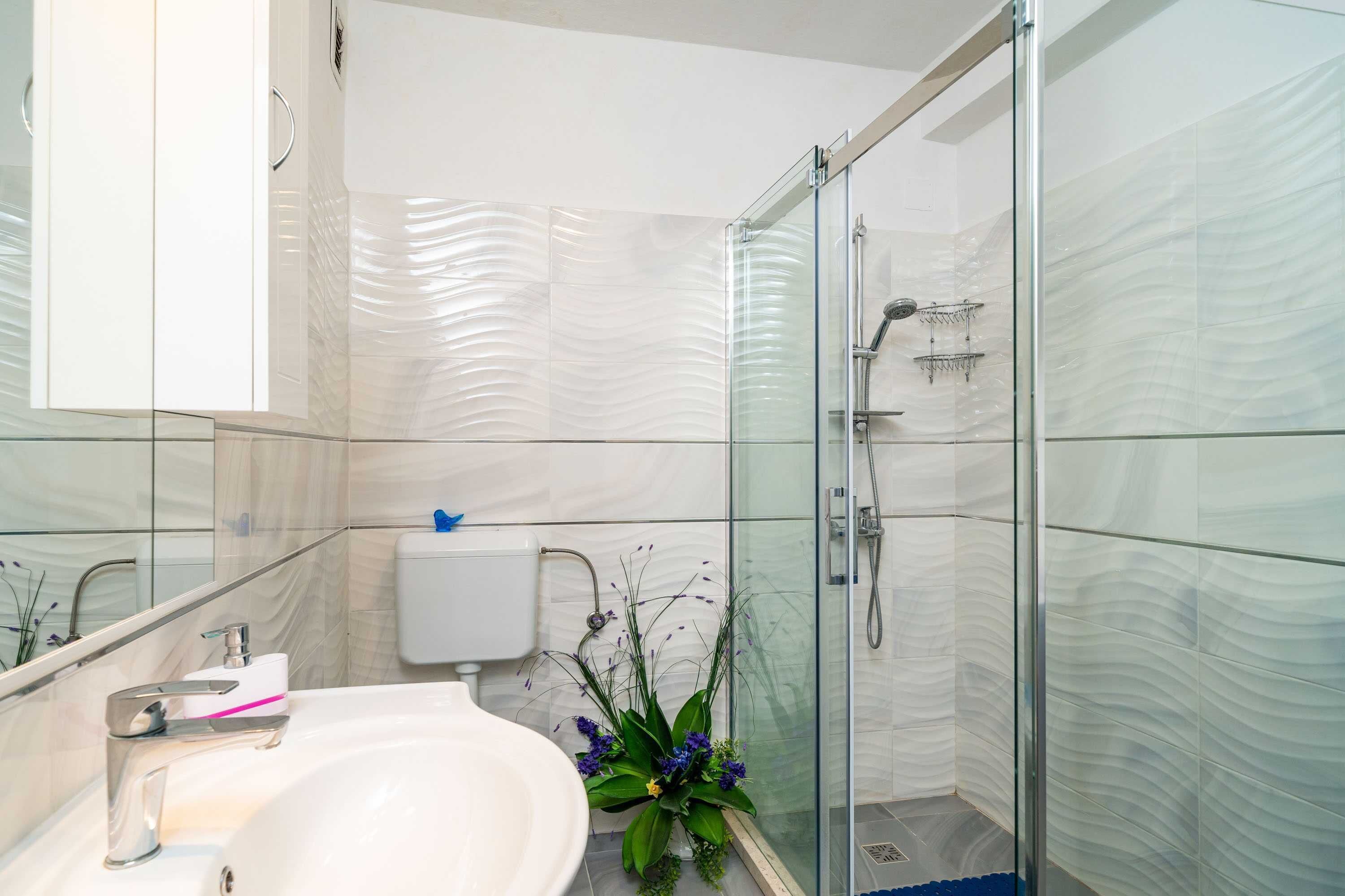 Un baño moderno con cabina de ducha de vidrio, un lavabo blanco y un inodoro.