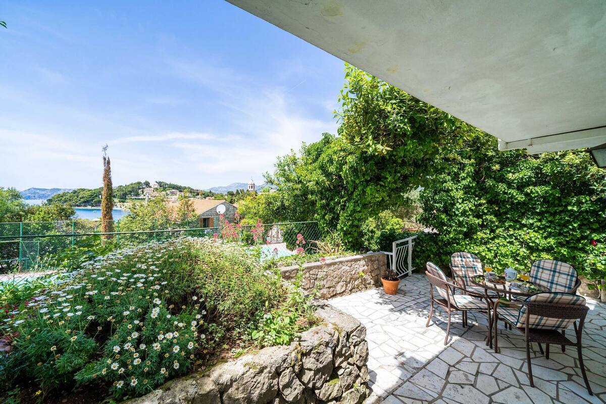 A patio with outdoor furniture and a view of a hillside with greenery and a building in the distance.