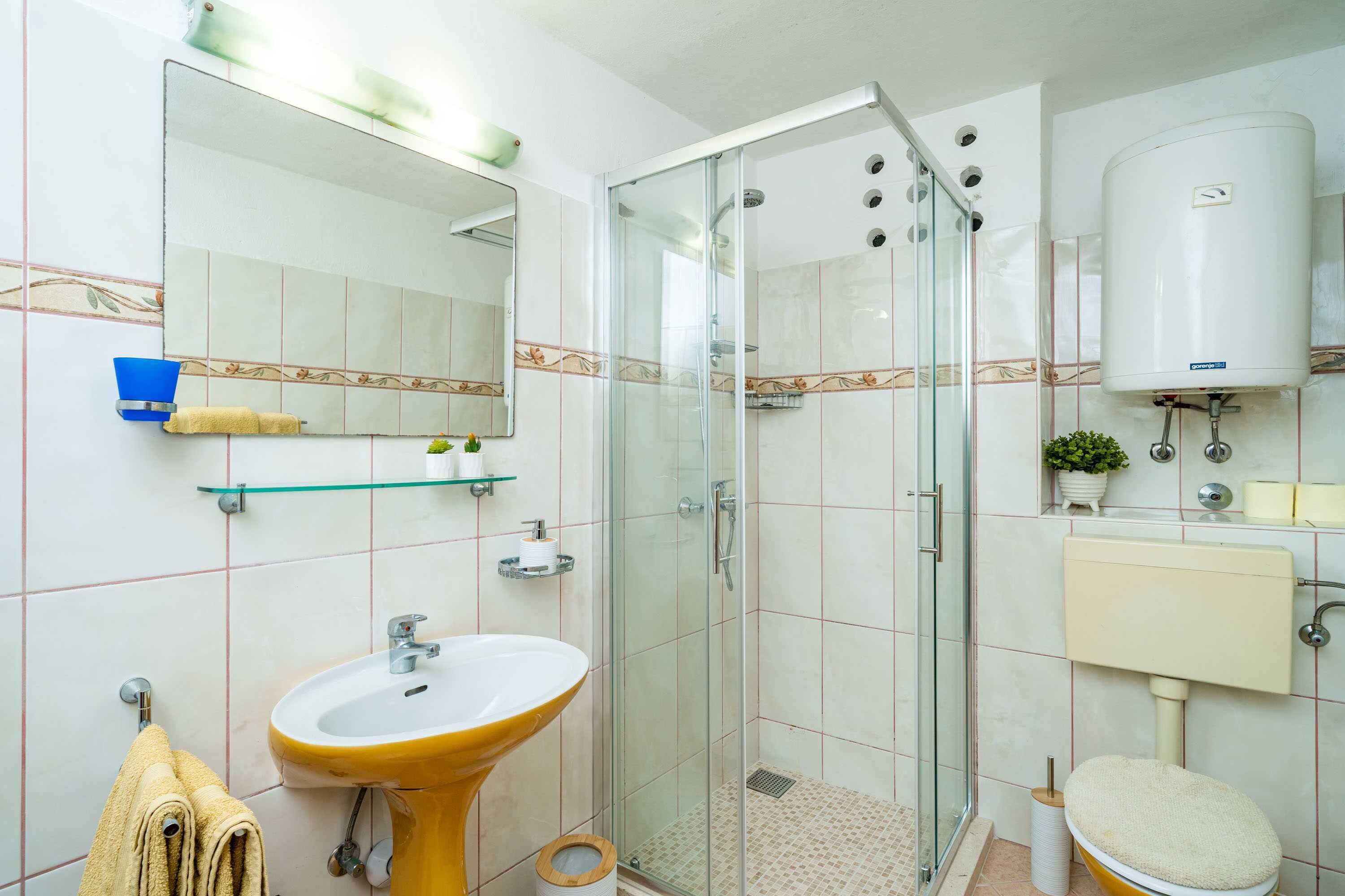 Un baño con ducha envuelta en vidrio, lavamanos, inodoro y espejo.