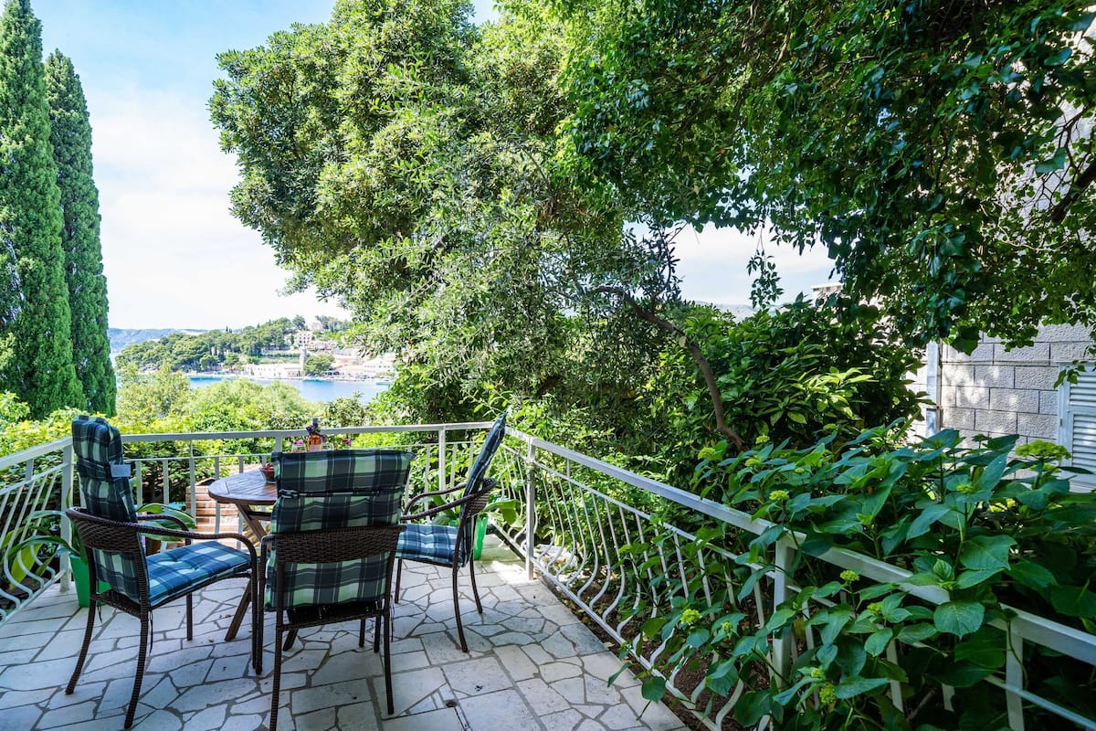 A patio with wicker chairs and a table, overlooking a scenic view of a lake and greenery.