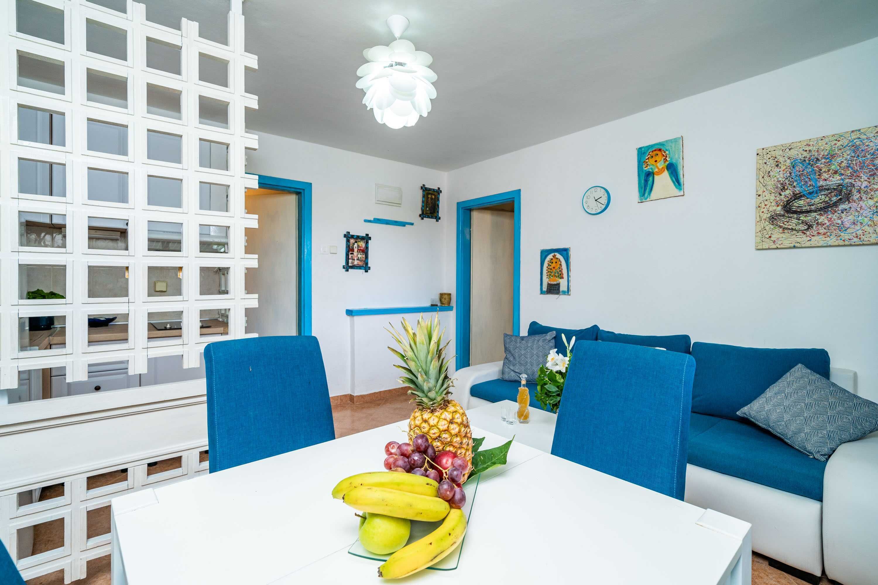 Uma sala de estar moderna com uma mesa de jantar branca, cadeiras azuis, um sofá azul e uma abacaxi sobre a mesa.