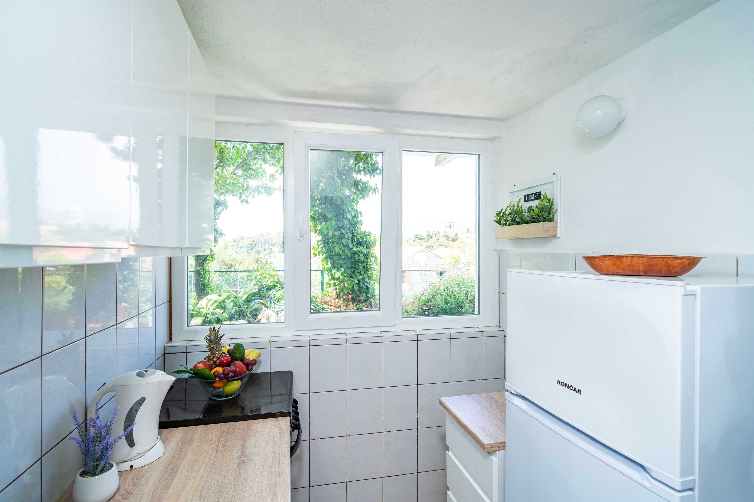 A modern kitchen with white cabinets, a white refrigerator, a wooden countertop, and a window with a view of greenery.