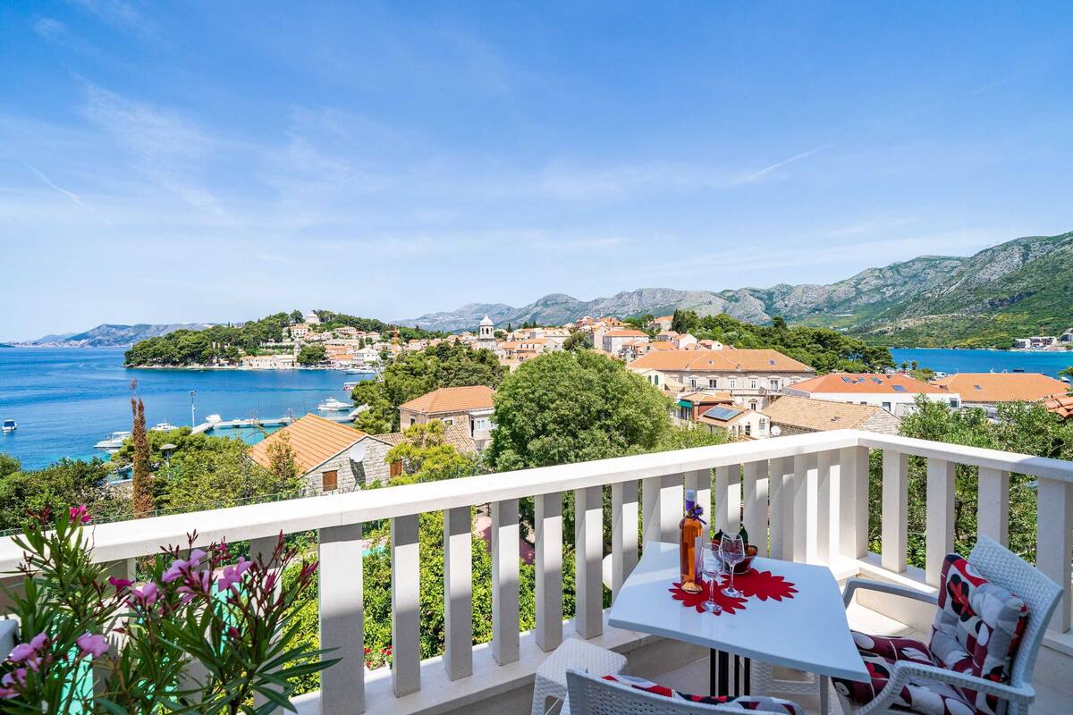 A balcony with a white railing, a table with a red tablecloth, and a chair.
