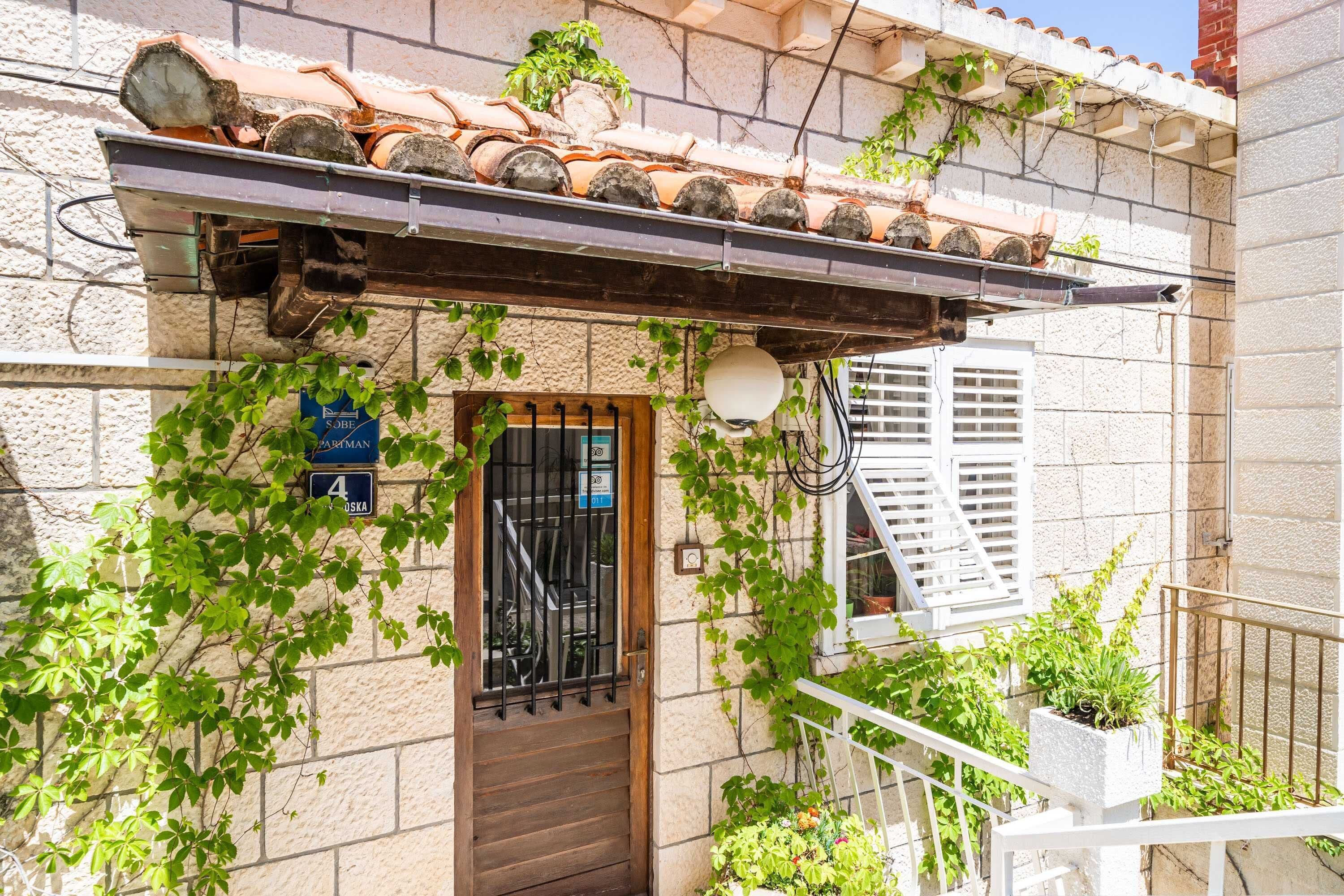 A building with a tiled roof, a wooden door with a metal gate, and a balcony with potted plants.