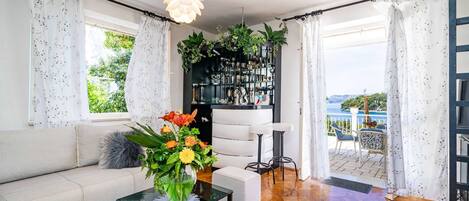 Una sala de estar moderna con un sofá, una mesa de centro con un jarrón de flores, una estantería y vistas al exterior.