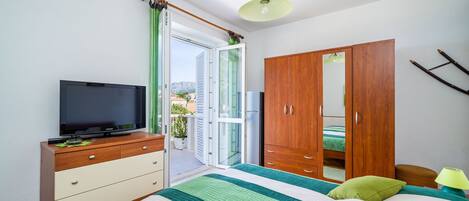 Un dormitorio con cama, televisor en una cómoda, armario y puerta corrediza de vidrio a un balcón.