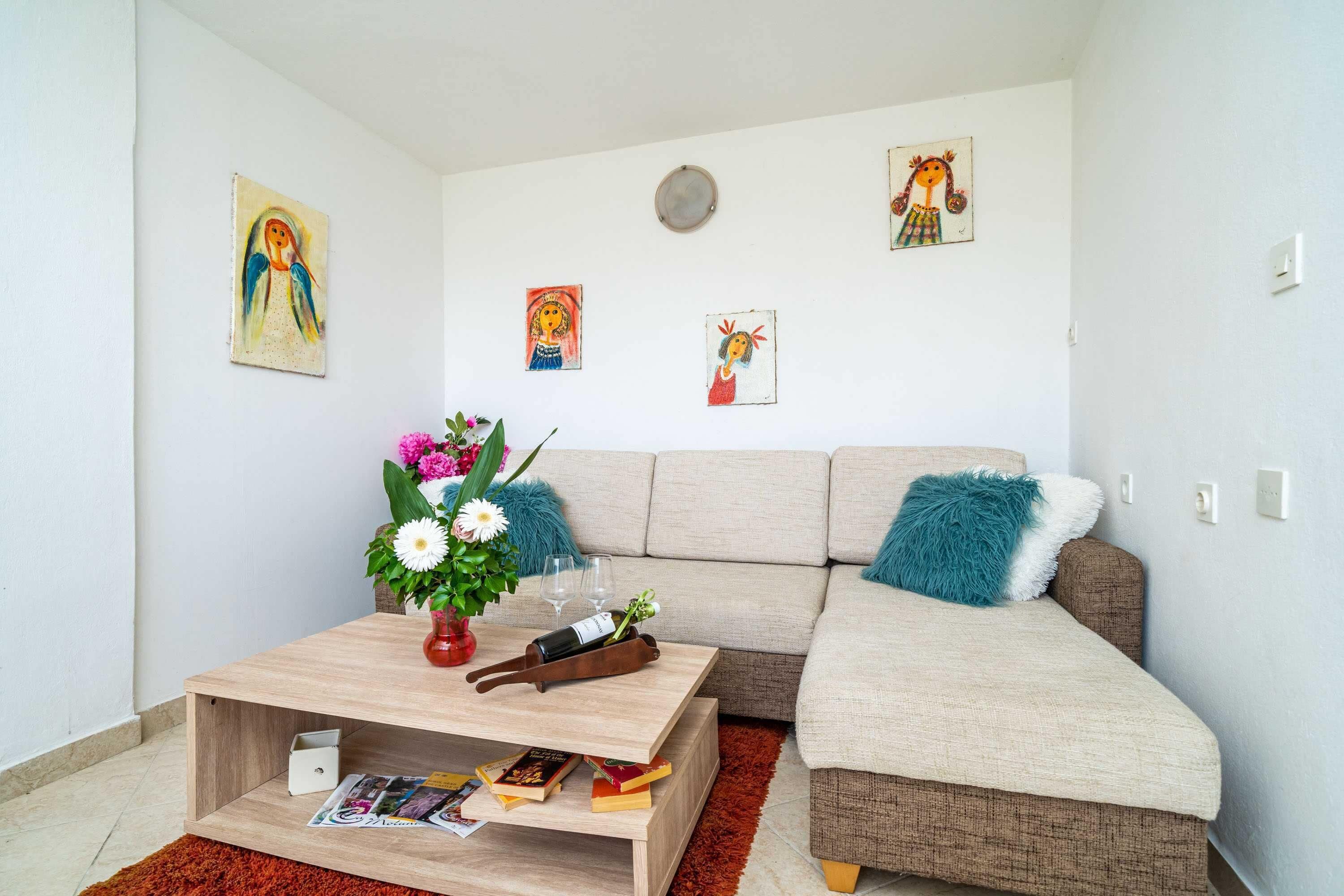 Een woonkamer met een bank, een bijzettafeltje met boeken en een bloevas, plus wanddecoratie.