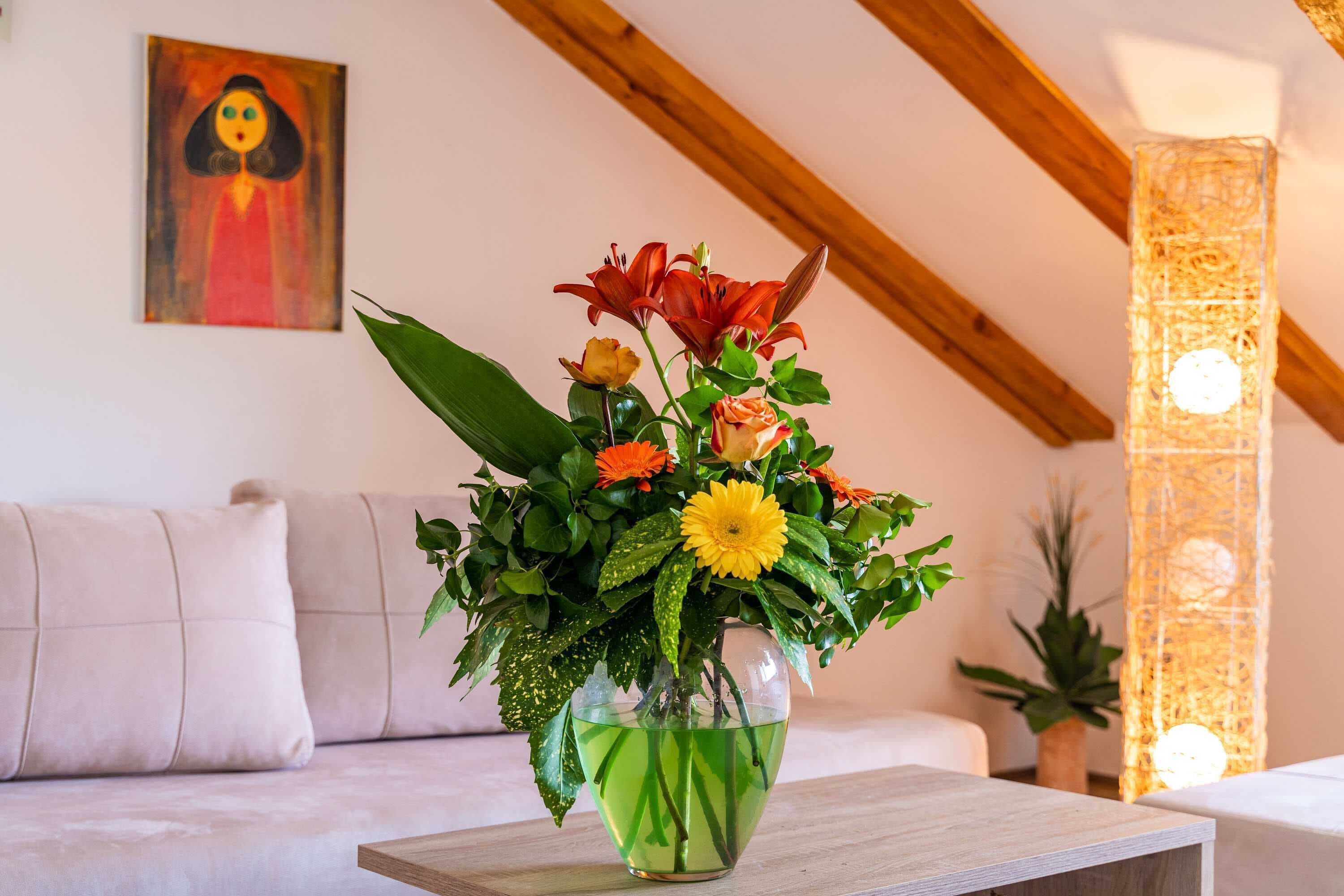 Una stanza con un divano, un vaso con fiori e un quadro appeso al muro.