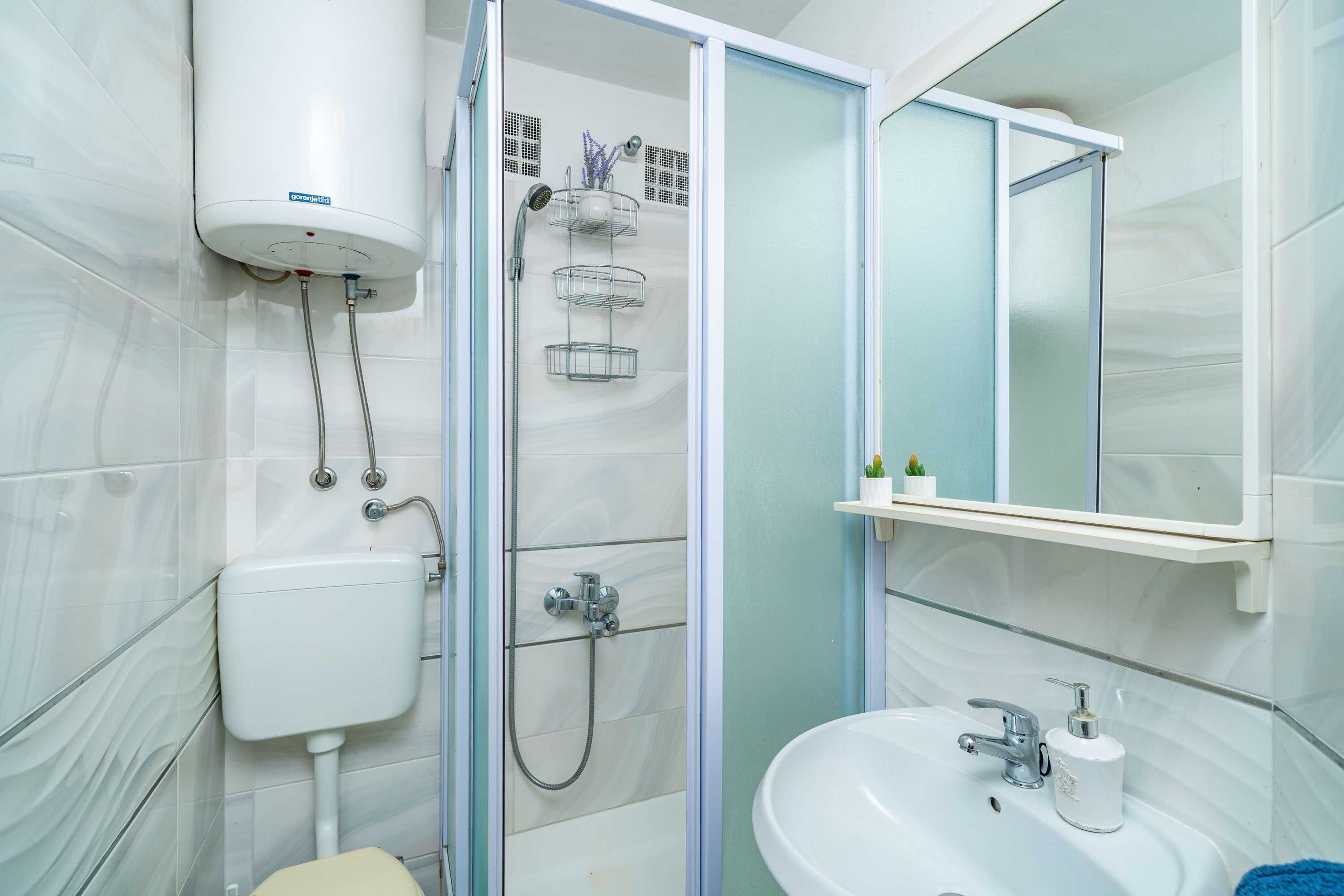 A bathroom with a toilet, sink, shower, and a mirror.