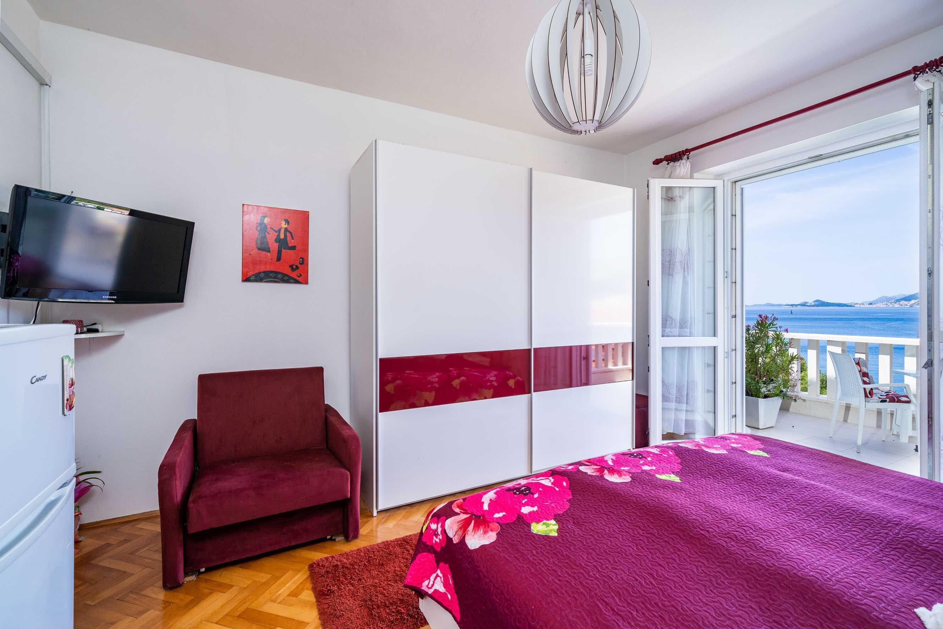 Ein Schlafzimmer mit Bett, einem roten Sessel, einem Kleiderschrank, einem Fernseher und einem Balkon mit Meerblick.