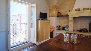 A kitchen with a wooden table, a television, a fireplace, and a view through a window with a balcony. - Holiday Home 'Dimora Storica Maruggio' with Terrace & A/C (maruggio)
