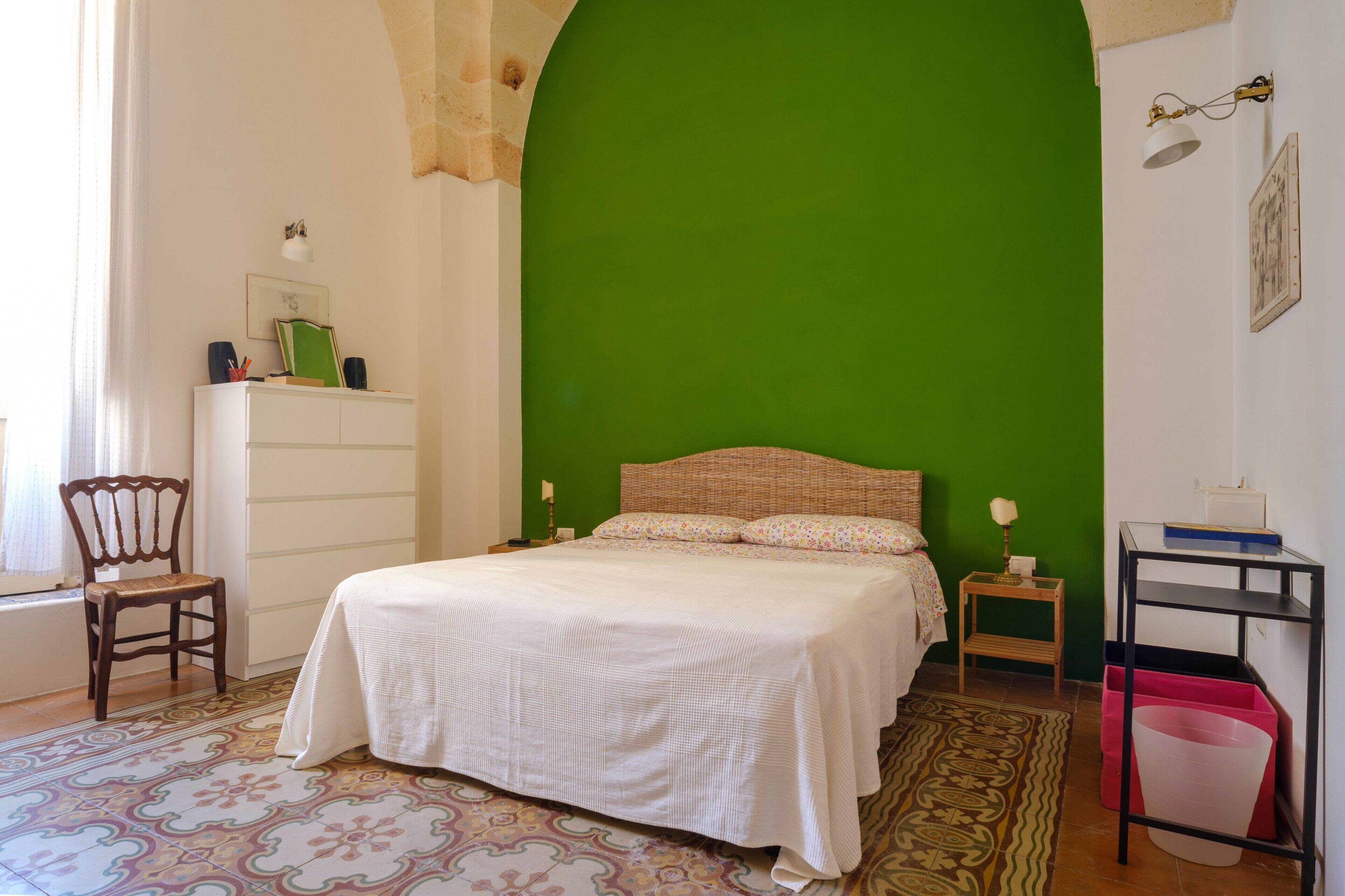 Une chambre à coucher avec un lit, une chaise, une table de chevet, une lampe, une étagère et un mur vert.