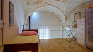 A bedroom with a wooden bed, a white desk, a chair, and a stone wall. - Holiday Home 'Dimora Storica Maruggio' with Terrace & A/C (maruggio)