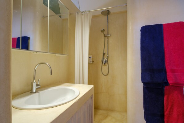 A bathroom with a sink, mirror, shower, and towels.