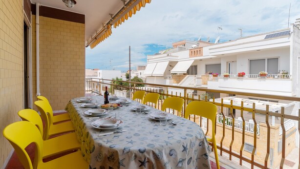 A balcony with a dining table set for four, yellow chairs, and a view of neighboring buildings. - Apartment Casa LILLI 11 posti Near the Sea with Sea View, A/C & Balcony (santa maria al bagno)