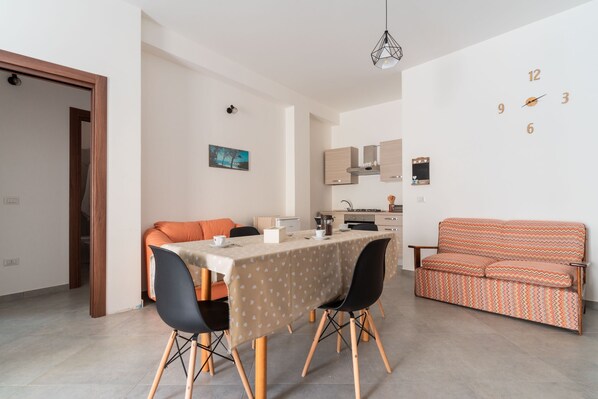 A modern living room with a sofa, dining table, chairs, and a kitchen area.