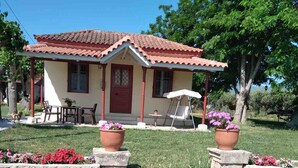 Une maison avec un toit recouvert de tuiles rouges, une véranda avec une chaise suspendue et un petit jardin agrémenté de plantes en pot.